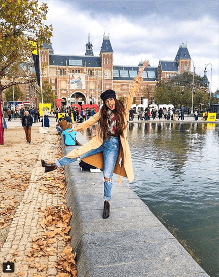 Blogger Pallavi Rhuail wearing yellow trench coat standing on ledge of pond