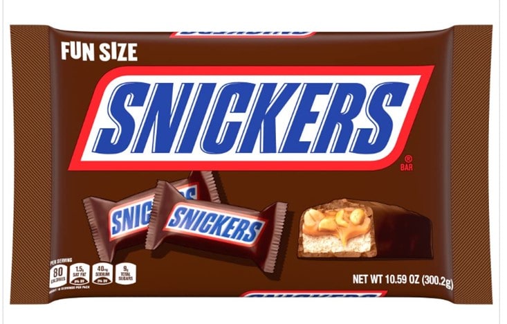 A brown 10.59oz bag of fun size snickers with the Snickers logo on the top, two unopened snickers bars on the left, an open and cut bar on the right, showing the nougat, and caramel and peanut filling 