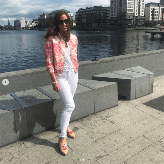 Blogger Naomi Clarke wearingpink floral bomber jacket and white pants in front of river
