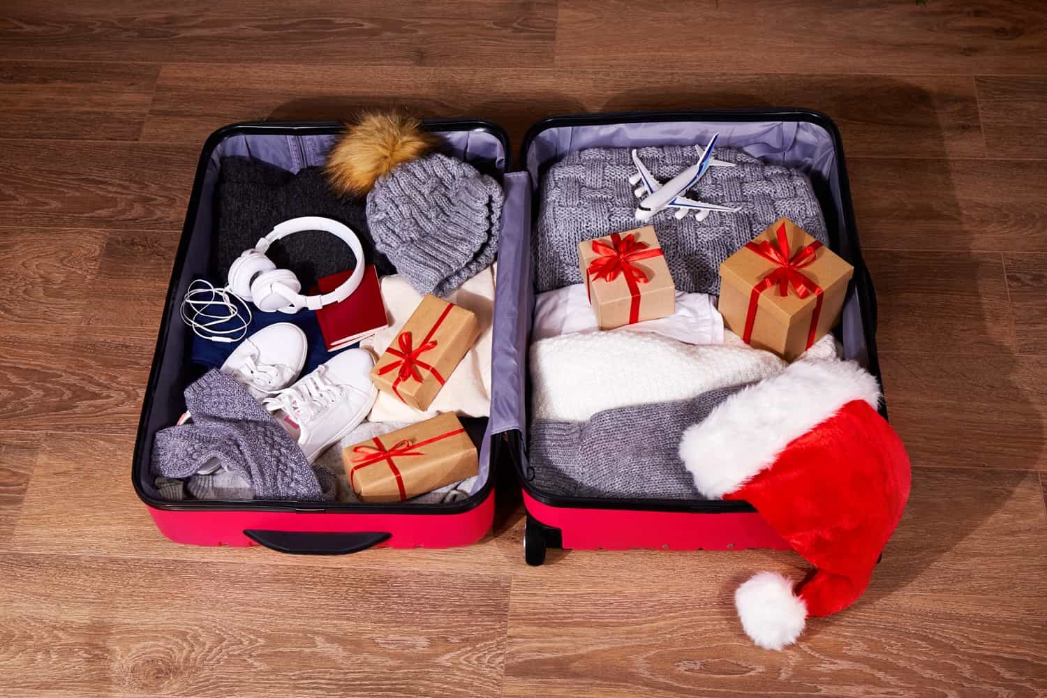open suitcase packed with winter clothing, wrapped presents, and a holiday hat