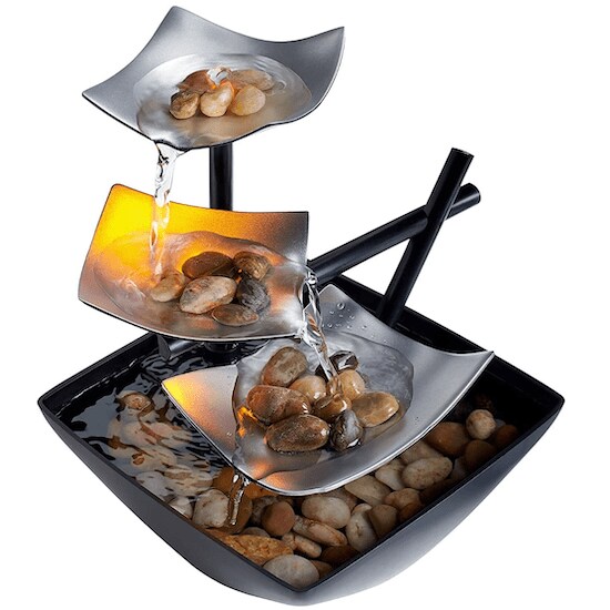 A silver and black HoMedics Indoor 3-Tier Relaxation Tabletop Fountain with several clumps of tan, brown, and beige rocks and running water