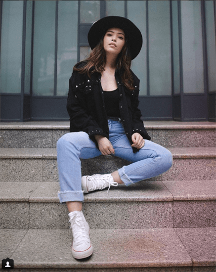 Influencer Lilia Cortes sitting on steps in jeans and black hat