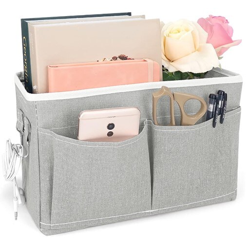 A gray bedside organizer containing a couple of books, a notebook, and a couple of roses in the large compartment, and a phone and scissors and two pens in the small, separate ones