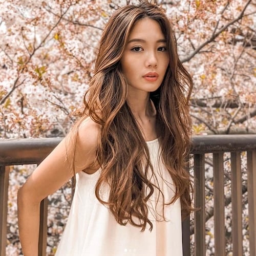 Reiko McNish Sato posing in a white dress in front of railings and trees