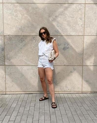 Canadian influencer Allana Davison in  a white shot-sleeve button down, cut-off shorts, and slip-on sandals