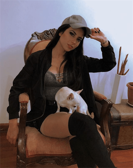 Influencer Balentina Villagra sitting in chair wearing hat and over the knee black boots with tiny dog on lap