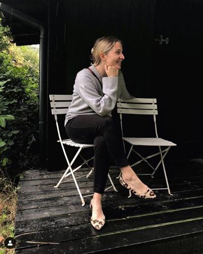 Danish influencer Signe Hansen sitting outdoors in black pants and a gray sweater