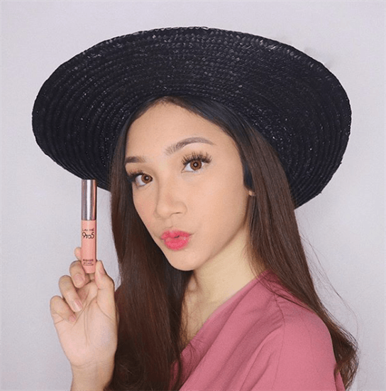 Influencer Stefany Visa wearing black straw hat and holding up pink lipstick