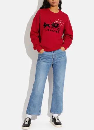 an image of a woman wearing a red coach sweatshirt with a graphic of a rabbit leading a carriage from Coach