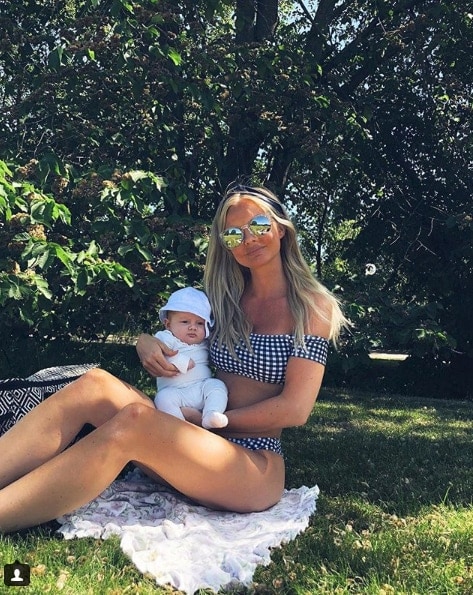 Influencer Alexandra Bring in swimsuit on grass holding baby