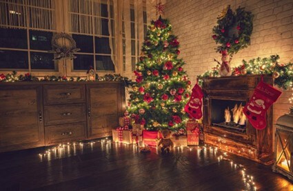 Cozy nighttime living room scene of an illuminated Christmas tree beside a roaring fireplace 