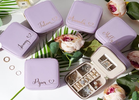 Five closed lavender jewelry boxes personalized with the recipients’ names on them and an open lavender box showing the organized jewelry inside