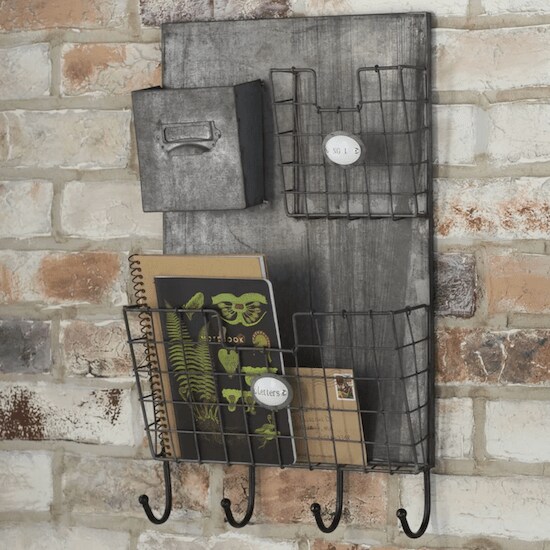 A grey wooden Wildon Home Wall Organizer with four key hooks and three baskets holding notebooks and mail in front of a brick wall