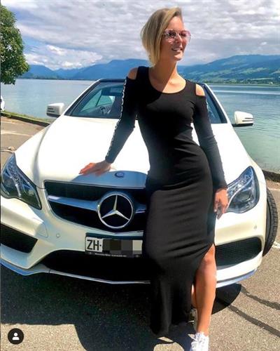 Swiss influencer Edaa posing against a white Mercedes in a black maxi dress