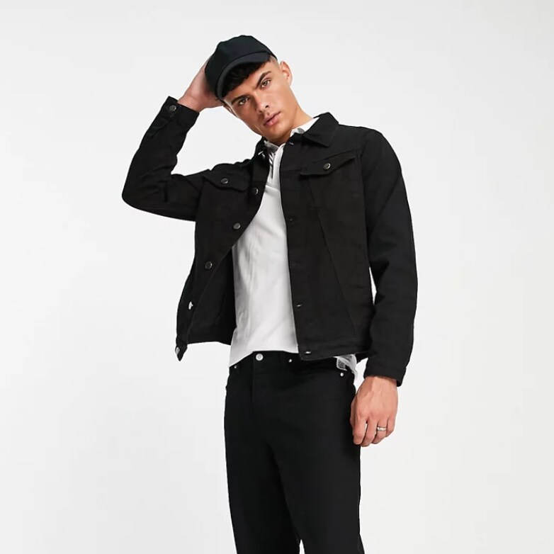 A man wearing a black Another Influence Denim Jacket with a white polo, black baseball cap,  and black pants