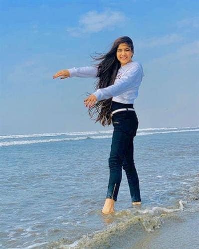 Pakistaini influencer Reeja Jeelani playing in the ocean surf in jeans and a hoodie