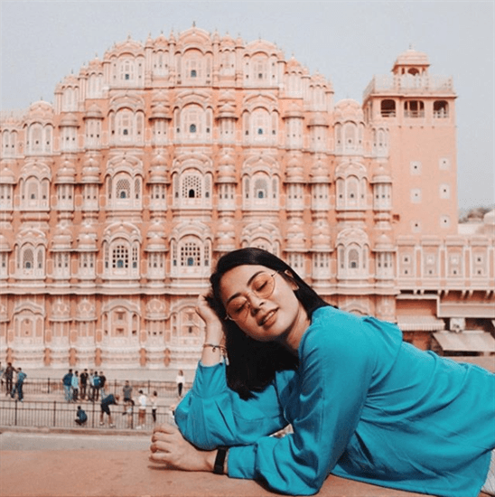 Influencer Andra Alodita leaning on ledge wearing blue shirt in front of famous building