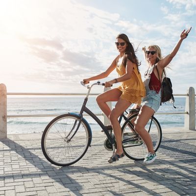 two girls riding a bicycle on a beach boardwalk