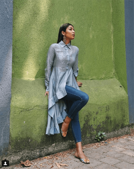 Blogger Santoshi Shetty wearing long sleeve blue tunic with jeans leaning on green wall