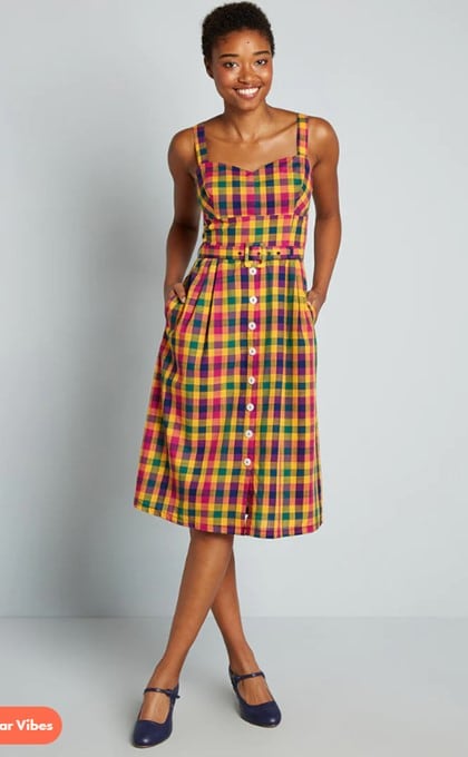 Short-haired model posing before a wall with her hands in the pockets of the colorful Check My Pulse Fit and Flare dress, and her legs crossed in navy flats with straps