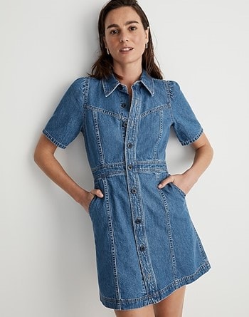 Model leaning on a white wall, dressed in Madewell’s denim puff-sleeve mini dress with her hands in the pockets