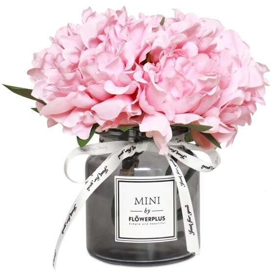 A glass jar filled with artificial pink peonies, decorated with a white ribbon and a square sticker with the business’ name on it
