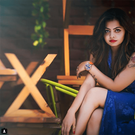 Blogger Shivali sitting wearing blue mesh dress and orange strapped watch