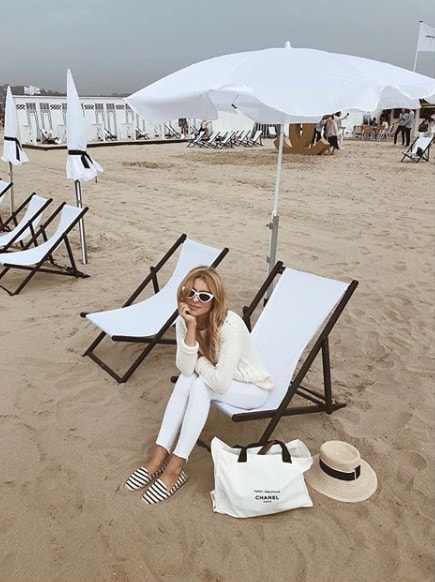 Influencer Katarzyna Tusk wearing all white sitting on chair on the beach under white umbrella