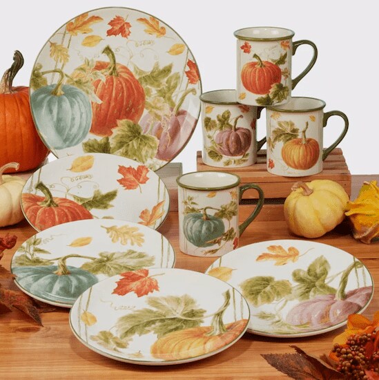 A 16-Piece Certified International Autumn Harvest Dinnerware Set featuring pumpkin print plates and cups in the middle of a wooden table