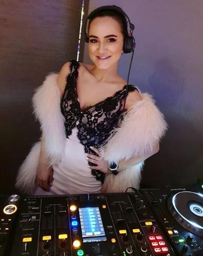 DJ and influencer Katrin Love posing behind her soundboard and wearing headphones and a pink boa