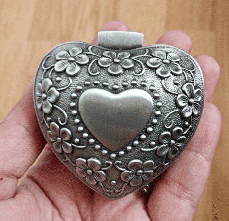 A hand holding the palm-sized heart-shaped jewelry box with vintage floral engraving