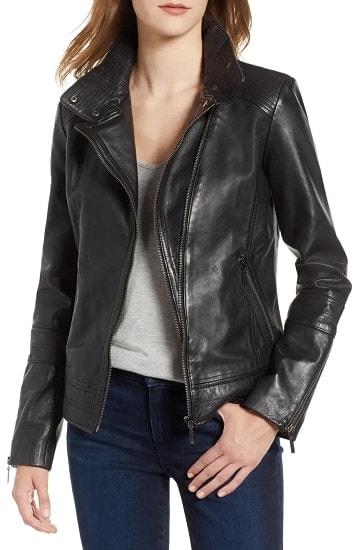 A model wearing a black leather moto jacket with a grey tank top and blue jeans