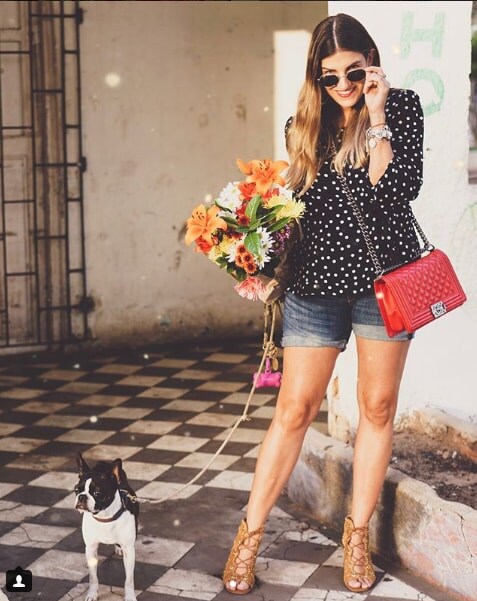 Blogger Laura Echavarria carrying flower bouquet and small dog on lease standing on checkered floor