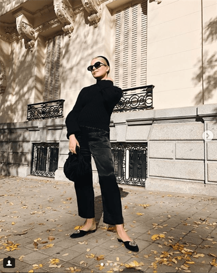 Influencer Trini Gonzalez wearing black turtleneck and black shiny pants with black slip on shoes