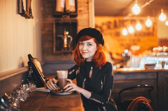 Blogger Rebecca sitting at coffee shop holding drink and wearing beret