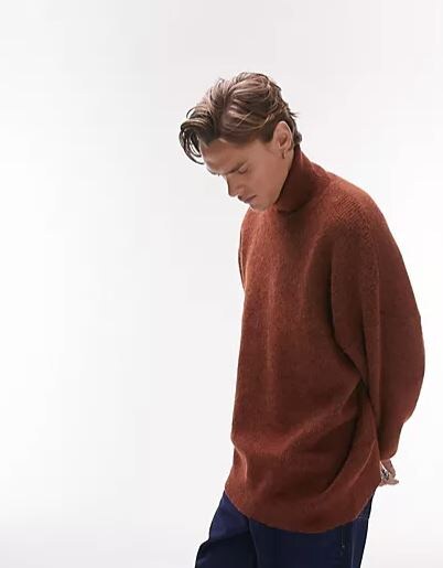 blonde man wearing a brown knitted sweater with blue jeans
