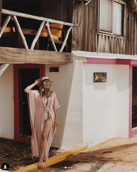 Influencer Christianne Sandoval wearing white and brown striped swimsuit with pink floor length cover up