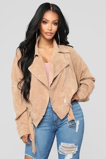 A model wearing a camel-colored cotton moto jacket with a pink top and ripped jeans