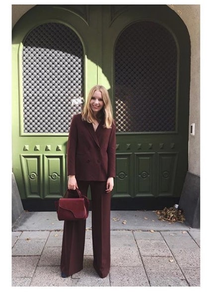 Influencer Carolina Storm posing in maroon pant suit in front of green wall