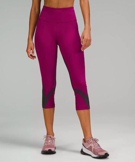 A woman wearing a pair of Magenta Purple/ Graphite Grey Throwback Inspire High-Rise Crop 21-Inch Leggings with pink and white gym shoes