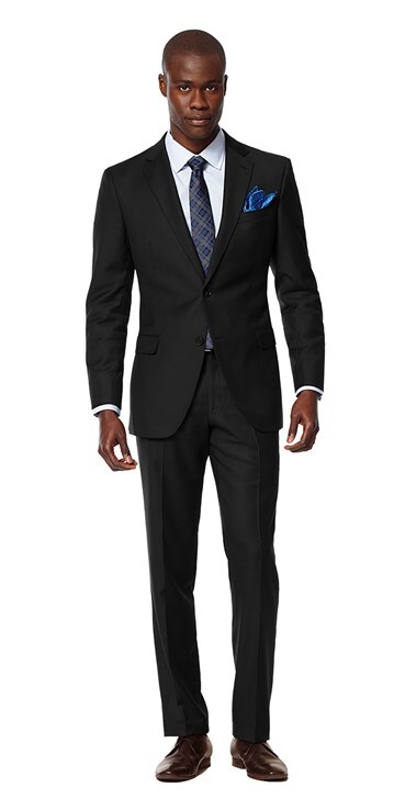 Model dressed in Black Lapel’s solid charcoal suit, paired with classic dark brown shoes, a navy silk handkerchief, and a blue checkered tie.