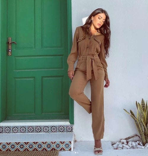 Alanoud Badr wearing a brown one-piece suit and silver sandals in front of a white wall and a green door with decorative stairsteps 