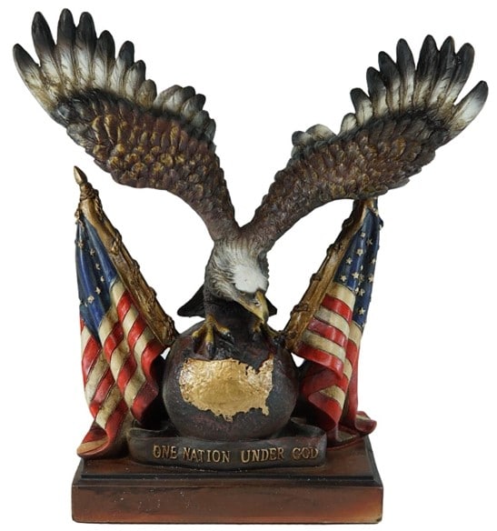 A sculpture of an American Bald Eagle with its wings spread, placed on top of a wooden stand with the US map and the words “One Nation Under God” engraved, and an American flag on each side