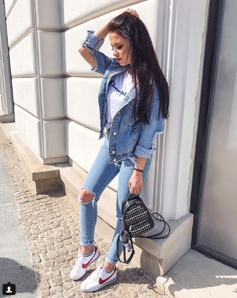 Influencer Karoline Grabowska wearing jean jacket and jeans leaning on white wall in nike shoes
