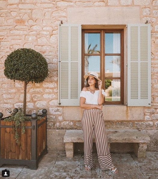 Influencer Nicole Falciani wearing straw hat and striped pants in front of window
