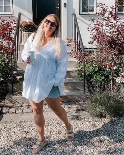 Danish influencer Christine “Acie” Egholm enjoying a coffee in shorts and a white tunic
