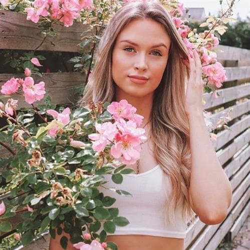 Danish lifestyle blogger Laura Leth posing by a wooden fence covered with pick roses