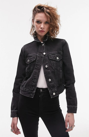 A woman wearing a Washed Black Topshop Tilda Crop Denim Jacket with a white shirt tucked into a pair of black denim pants
