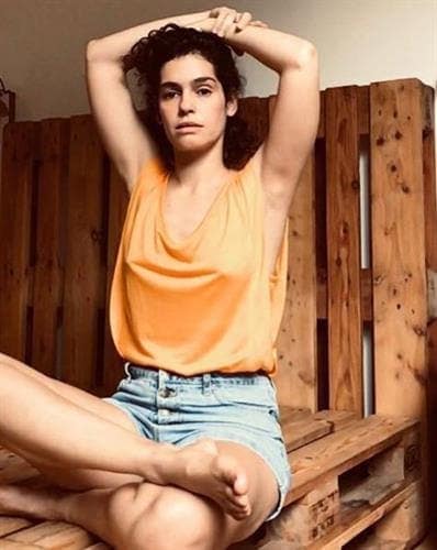 Brazilian actress and influencer Maria Flor sitting cross-legged in a tank top and denim shorts