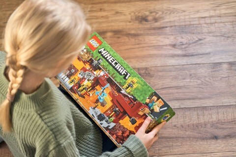 A young girl looks down at a boxed Lego Minecraft set she holds in her hands